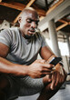 Phone, fitness and sweat with a black man athlete checking his social media after a workout or exercise at the gym. Training, mobile and health with a male tracking his progress on an internet app