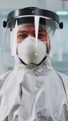 Wall Mural - Vertical video: Portrait of scientist man wearing coverall smiling at camera sitting in modern equipped laboratory. Chemist doctor xamining virus evolution using high tech for scientific research