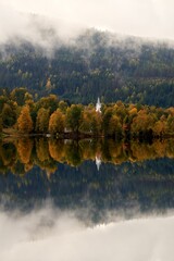 Wall Mural - Aerial view of church surrounded by autumn dense trees and water in Norway