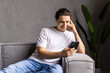 © F8  \ Suport Ukraine - Portrait of an attractive smiling young man wearing casual clothes sitting on a couch at the living room, using mobile phone
