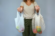 © David Pereiras - Unrecognizable woman comparing reusable mesh bag and disposable plastic bag with fruits inside over grey background. Sustainable lifestyle and zero waste concept.