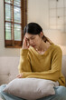 © NanSan - Asian woman with a headache and stress while sitting on the sofa at home