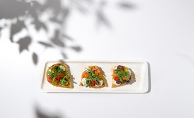 Canvas Print - Aesthetic composition with salmon bruschetta on white background with shadows from flowers. Italian bruschetta with salmon, avocado, cheese and olives on fine dining in summer. Elegant menu concept.