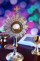 Wall Mural - Catholic religion concept. Catholic symbols composition. The Cross, monstrance,  Holy Bible, rosary and golden chalice on blue bokeh background. 