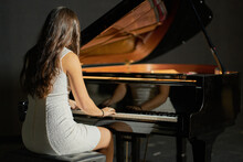 A Woman With Brown Hair Dressed In A White Dress Playing A Black Grand Piano With The Lid Raised