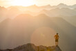 © Cavan Images - Trail runner standing on edge of a mountain cliff at sunset.
