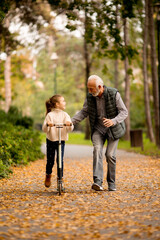 Wall Mural - Senior man teaching his granddaughter how to ride kick scooter in park