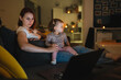 © Miljan Živković - Small caucasian child little girl toddler mother and daughter sitting in dark room at night at home on sofa bed watching cartoons or movies on laptop computer real people family growing up copy space