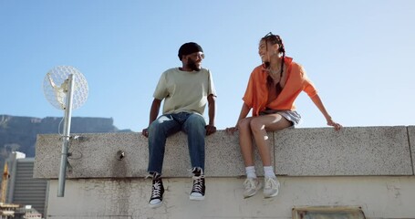 Canvas Print - Friends, fist bump and happiness on city building rooftop together talking, conversation and laughing, urban lifestyle. Couple, man and woman do cool greeting sitting outdoor to relax with cityscape