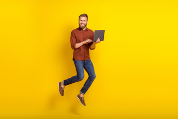 Poster - Full length photo of optimistic funny man masculine beard dressed burgundy shirt hold laptop flying isolated on yellow color background