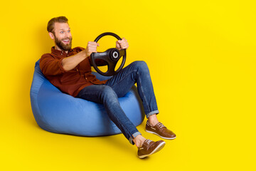 Wall Mural - Full length photo of overjoyed person sit bag hands hold wheel look empty space isolated on yellow color background