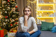 © Liubomir - sad Woman alone at home for Christmas and New Year, sitting depressed near Christmas tree on sofa in living room, waiting for celebration.