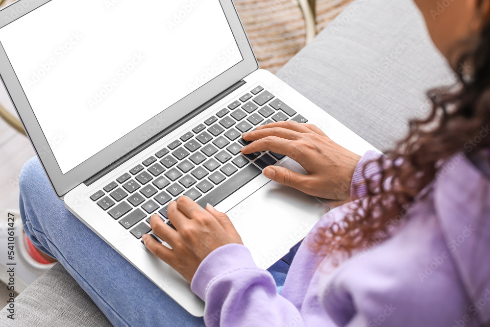 Young woman using laptop on sofa at home, closeup