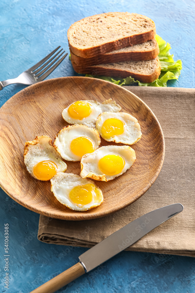 Wooden plate with fried quail eggs on color background, closeup
