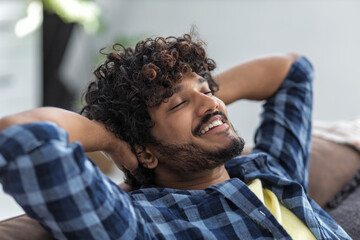 Relax at home, positive thinking concept. Portrait of happy asian man lying on sofa resting. Young male throwing his hands behind his head thinks of something good and smiles