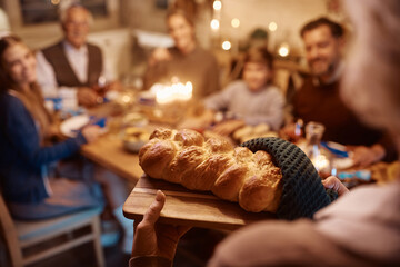 Close up of senior woman serving Challah bread to her family during dinner on Hanukkah.