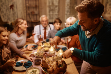 Wall Mural - Happy man carving roast turkey during Thanksgiving meal with his extended family.