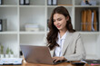 © PaeGAG - Happy businesswoman typing on laptop at her desk looking at camera in bright office