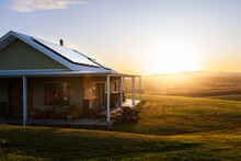 Homestead On Hilltop With Last Rays Of Sunlight Shining Over Scene And Solar Panels On Roof