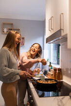 Two Women Laughing As They Cook Together At Home