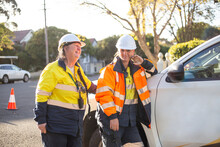 Two Smiling Women Road Workers With White Helmet And High Vis Workwear Leaning On A White Car