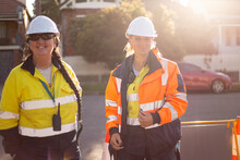 Two Smiling Women Road Workers Wearing White Helmet With High Vis In Afternoon Light