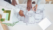 © J Bettencourt/peopleimages.com - Top view, teamwork and architects hands on blueprint, model or building, architecture or construction project. Team, engineers and group planning development project, design sketch and tablet mockup