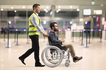 Poster - Airport worker pushing a man in a wheelchair inside the airport terminal building