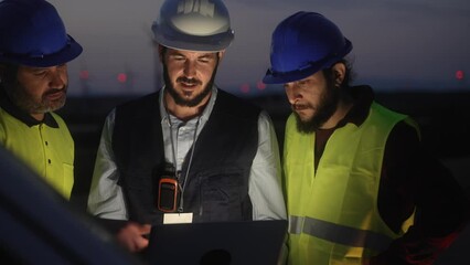 Wall Mural - Electrical Engineer and technical industry workers discussing project of electricity wind power station, planing renewable energy factory at night 