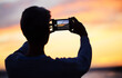 © David L/peopleimages.com - Man silhouette, smartphone and beach sunset photograph for social media post. Young photographer man, vacation travel adventure or holiday freedom trip by ocean sea memory on mobile technology app