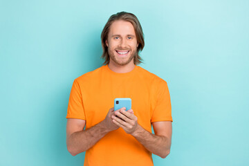 Wall Mural - Photo of young attractive handsome funny student guy hold phone addicted blogger online work positive smile isolated on blue color background