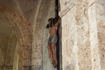 Wall Mural - Old wooden crucifix with peeling paint against grungy dirty stone wall background in church.  Religious heritage conservation problem concept.