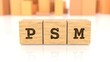 Word PSM branded on wooden cube blocks reflected on the shiny table. Business concept. In the back are wooden cuboids in various shapes. (3D rendering)