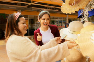 Happy two female friends shop for trendy fashionable sun protection hats for women at a convenience store inside stylish gas station : Travel holiday vacation concept