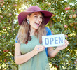 © J Maas/peopleimages.com - Woman, fruit farm and open store sign of a happy entrepreneur for agriculture and apple orchard. Female manager proud and success smile with sustainable, eco friendly ecology and green farming trees