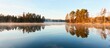 Panoramic view of the forest lake at sunrise. Soft golden sunlight, clear blue sky, reflections on water, fog, frost. Mighty trees. Finland. Nature, seasons, ecology, environment, eco tourism themes