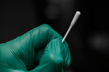 Close up on a gloved hand of a doctor or a nurse holding a covid test swab. Blurred dark background