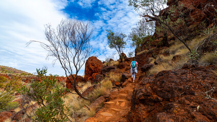 backpacker girl hiking on red rocks up a steep mountain in karijini national park in western australia, desert landscape of australian outback