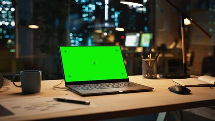 Fototapete - Laptop Computer with a Green Screen Chromakey Mock Up Display Standing on a Desk in the Office at Night. Modern Open Space Creative Agency with Manager Working in the Background.