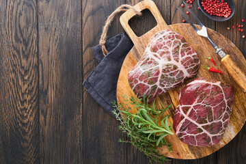 Steaks Raw. Raw cowboy steak, marbled beef meat with spices rosemary and pepper on black wooden board on old wooden dark table background. Top view. Mock up.