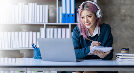 Young adult happy smiling Hispanic Asian student wearing headphones talking on online chat meeting using laptop in university campus or at virtual office. College female student learning remotely.
