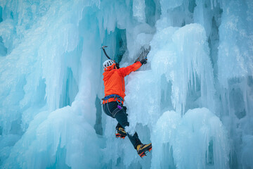 Alpinist man with ice climbing equipment on a frozen waterfall