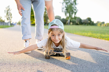  father pushing daughter lying on skateboard at park. Father and child girl have fun together.