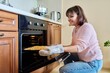 © Valerii Honcharuk - Middle-aged woman with cooked meat taking baking sheet out of oven