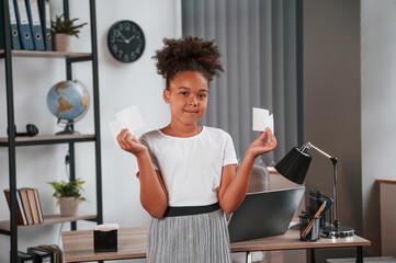 Wall Mural - Holding paper stickers. Cute african american child is standing in the domestic room