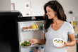 Beautiful young smiling pregnant woman taking healthy food from a refrigerator. Healthy eating during pregnancy. Fruits, dairy, and cereals.