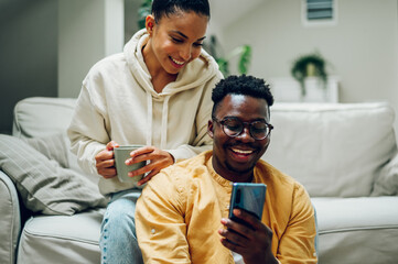 Multiracial couple at home while drinking coffee and using smartphone