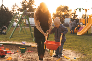 Mother and child playing with wheelbarrow in sandbox. Little builder. Education, and imagination, purposefulness concept. Support childhood parenthood symbol