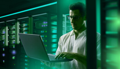 Man programmer. programmer sets up server hardware. Guy programmer in hosting provider building. Software developer. Man with glasses stands with laptop. IT developer career. IT engineer