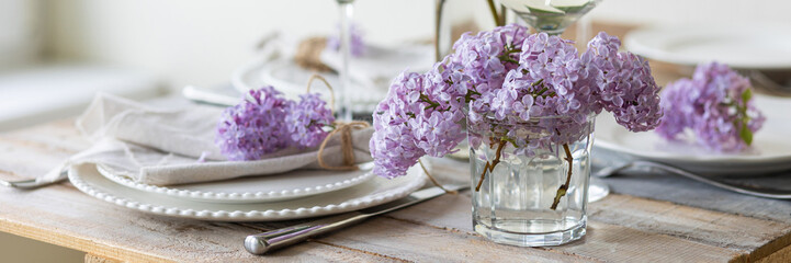 Beautiful table decor for a wedding dinner with a spring blooming lilac flowers. Celebration of a special event. Fancy white plates, and wineglasses. Countryside style. Banner